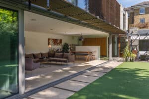 A modern home with a glass sliding door opens to a green lawn, showcasing an open-plan living and dining area furnished with contemporary pieces.