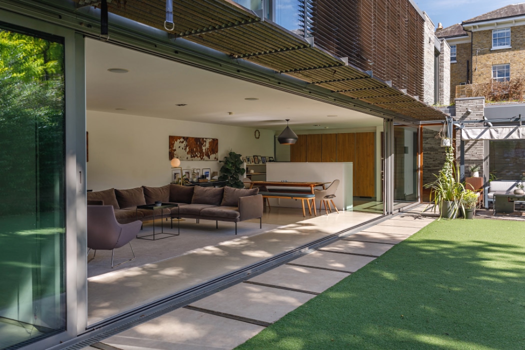 A modern home with a glass sliding door opens to a green lawn, showcasing an open-plan living and dining area furnished with contemporary pieces.