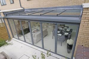 This glass-enclosed patio, seamlessly integrated with a brick house, features sliding doors on a stylish bifold door track. Inside, you'll find a cozy setting with a dining table and sofa for perfect relaxation.