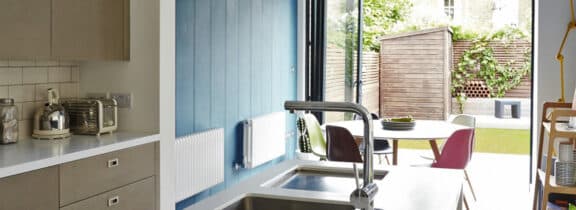 Modern kitchen with a sleek sink and countertop, blue accent wall, and bifold doors leading to a patio with outdoor seating, creating the perfect extension for indoor-outdoor living.