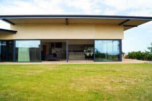 Modern house with large picture windows, flat roof, and a grassy lawn in the foreground.