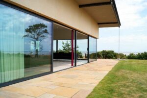 Modern house with expansive picture windows overlooking a grassy yard and distant trees.