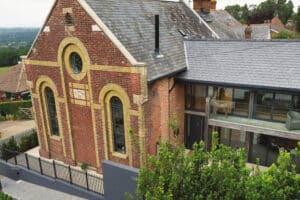 A converted brick chapel with large arched windows and a modern glass extension is set in a rural landscape.