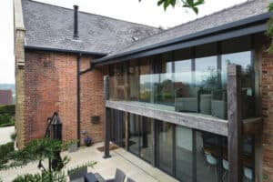 A modern two-story brick house with large glass windows and a balcony, featuring a patio with outdoor furniture.
