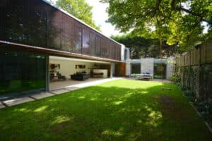 A modern house with expansive glass sliding doors opens onto a green lawn, where a wooden swing gently sways from a tree.
