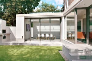 Modern house exterior featuring large glass windows and sliding aluminium doors, complemented by sleek white brick walls and a well-manicured lawn.