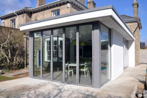 A sleek, flat roof extension with an overhang complements the older brick house, boasting large sliding doors that open to a stylish dining area.