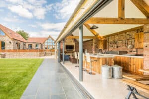 A modern rustic kitchen features sleek sliding aluminium doors that open to a patio with views of another building and a lush grassy area.