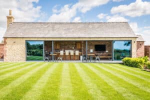 A modern building with sliding aluminium doors and a gray roof stands against a clear sky. It features a well-maintained lawn with perfectly striped mowing patterns.