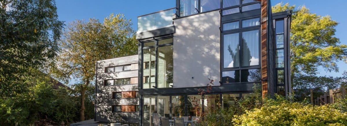 Modern house featuring large windows and aluminium bi-fold doors, complemented by a garden patio and surrounded by trees.