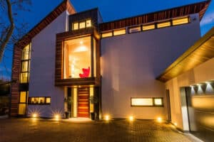 Modern house illuminated at dusk, featuring large windows, aluminium bi-fold doors, wooden accents, and a garage.