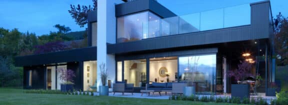 Modern two-story house with corner windows, a spacious balcony, and a well-lit patio.