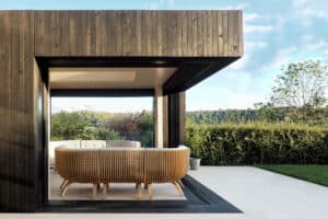 The modern outdoor seating area, enhanced by corner bi fold doors, features wooden furniture set against a scenic backdrop of greenery and a clear sky.