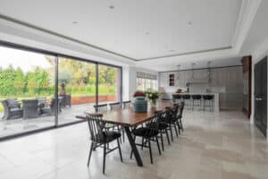 Spacious dining area with a long wooden table and sleek black chairs, offering a perfect view of the expansive patio through elegant glass sliding doors. In the background, the kitchen features a convenient counter complemented by stylish bar stools.
