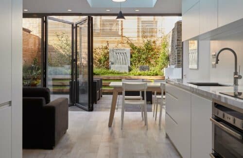 Modern kitchen with open bifold doors revealing a lush garden courtyard, flooded with natural light and green views.