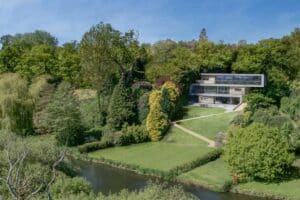 Modern house with large aluminium sliding doors and windows nestled in a lush, green landscape by a river.