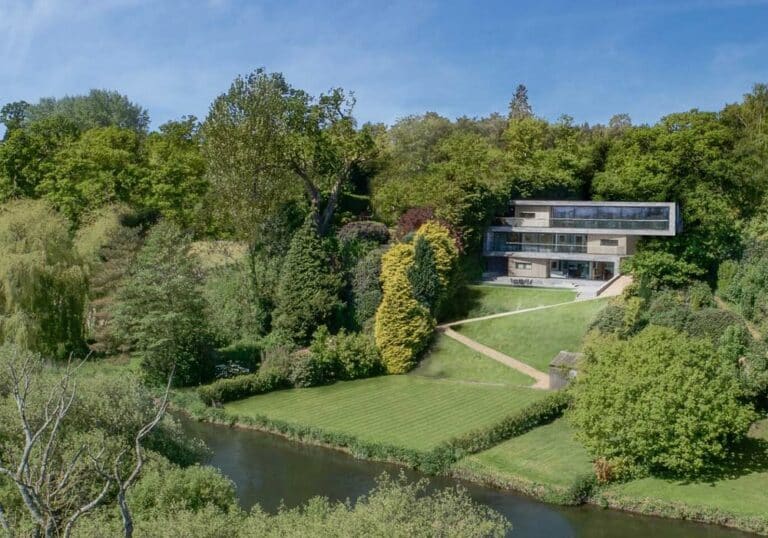 Modern house with large aluminium sliding doors and windows nestled in a lush, green landscape by a river.