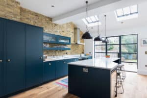 Modern kitchen with dark blue cabinets, white countertops, exposed brick wall, skylights, and a large island with bar stools. The space is beautifully complemented by aluminium heritage doors that add a touch of timeless elegance to the contemporary design.