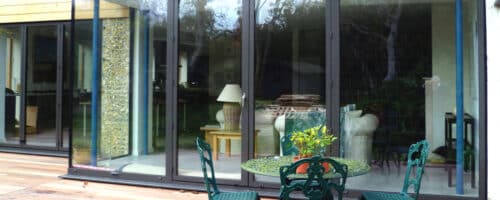 External glazed doors with slim aluminium frames opening onto a contemporary patio, showcasing seamless indoor-outdoor living with garden views.