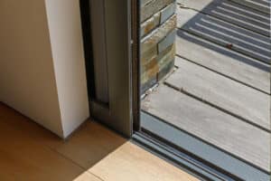 A corner sliding door partially open, showing the transition from indoor hardwood flooring to an outdoor wooden deck.