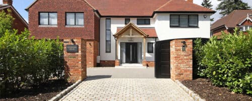 Modern home entrance featuring glazed external doors with slim-profile frames, brick pillars, and paved driveway approach.