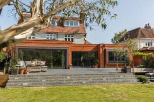 Spacious backyard with a modern patio, seating area, and well-maintained lawn, attached to a two-story house with large windows.