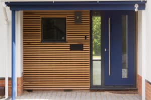 Modern entryway with wooden slat paneling, a rectangular window, and a navy blue door with vertical glass insert, under a blue canopy.