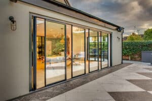 Modern house with expansive slide and turn doors opens to a spacious patio. Interior features elegant lighting and contemporary decor.