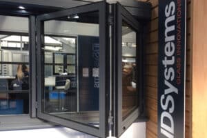 Folding glass door display in a showroom, featuring an IDSystems logo panel on the right and showcasing elegant aluminium bifold windows.