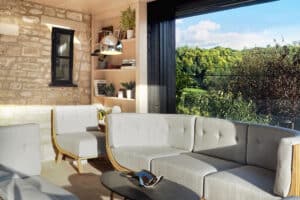 A modern living room with gray sofas, a black coffee table, and a floor lamp boasts pocket sliding doors that offer a seamless view of greenery through the large open window.