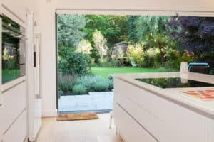 Modern kitchen with white cabinetry and an open pocket sliding door leading to a green garden with a shed.