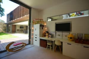Children's playroom with toys, a rocking horse, desk, and wall-mounted TV. Large pocket sliding doors open to a garden patio.