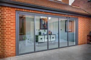 Modern slide and turn doors on a brick house reveal an interior with a decorative wall piece and furniture.