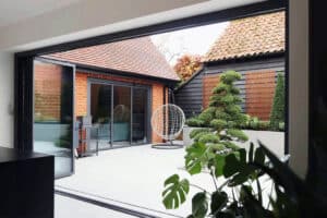 View of a modern courtyard featuring a round chair and well-trimmed trees, surrounded by brick and wood buildings. Large slide and turn doors seamlessly open to reveal the inviting space.
