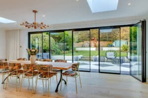 Dining room with a wooden table and patterned chairs, featuring elegant slide and turn doors that open to a garden with a playset and seating area.