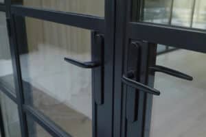 Close-up of a slide and turn glass door with black metal frames and handles. The interior behind the door is partially visible through the glass panes, adding a modern touch.
