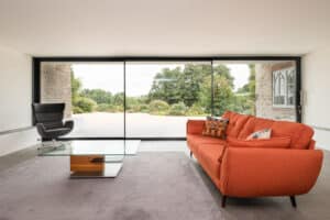 Modern living room with slimline sliding doors enhancing the large window view, featuring an orange sofa, a glass coffee table, and a gray armchair.