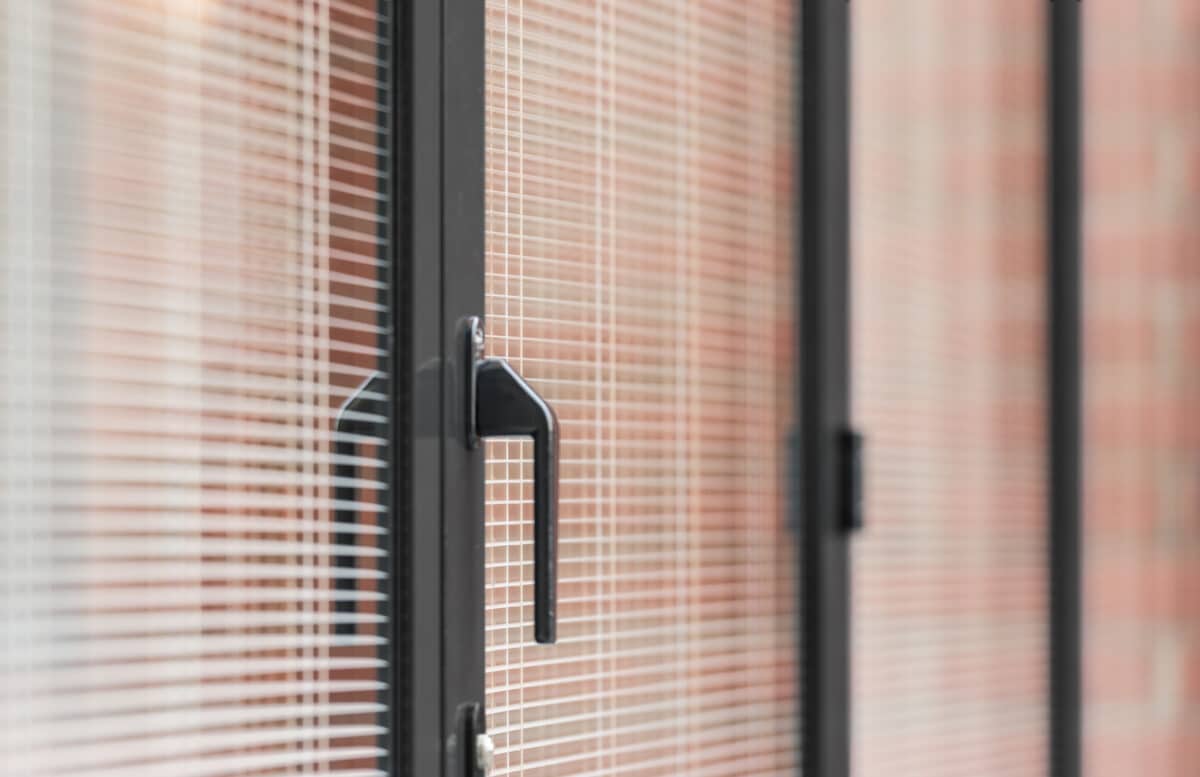 Modern aluminium sliding door with slim-profile frame and integrated handle, featuring decorative glazing pattern against brick backdrop.