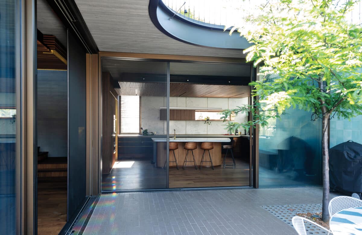 Contemporary open-plan kitchen with sleek aluminium sliding doors opening onto a paved courtyard, flooded with natural light.