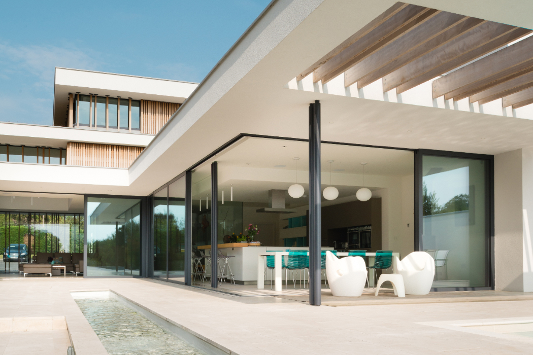 Modern white house with large glass windows, open patio with seating, and a small water feature.