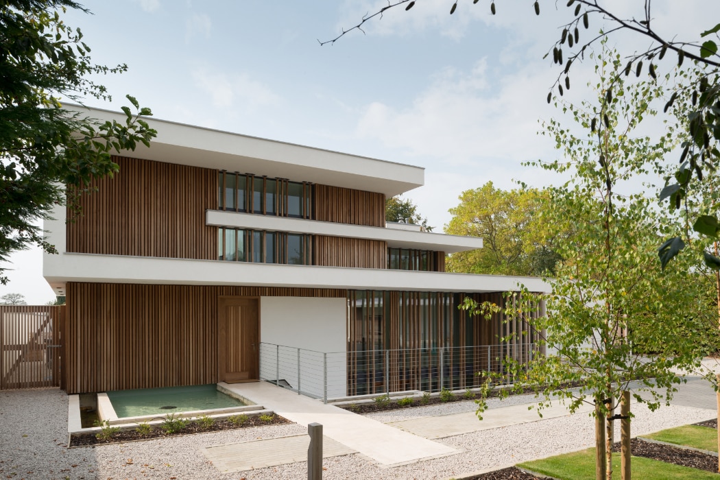 Modern multi-story house with wooden slat facade and large windows, set amidst a landscaped garden.
