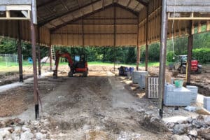 A construction site inside a large open structure features curtain walling alongside a small excavator, construction materials, and partially built walls.