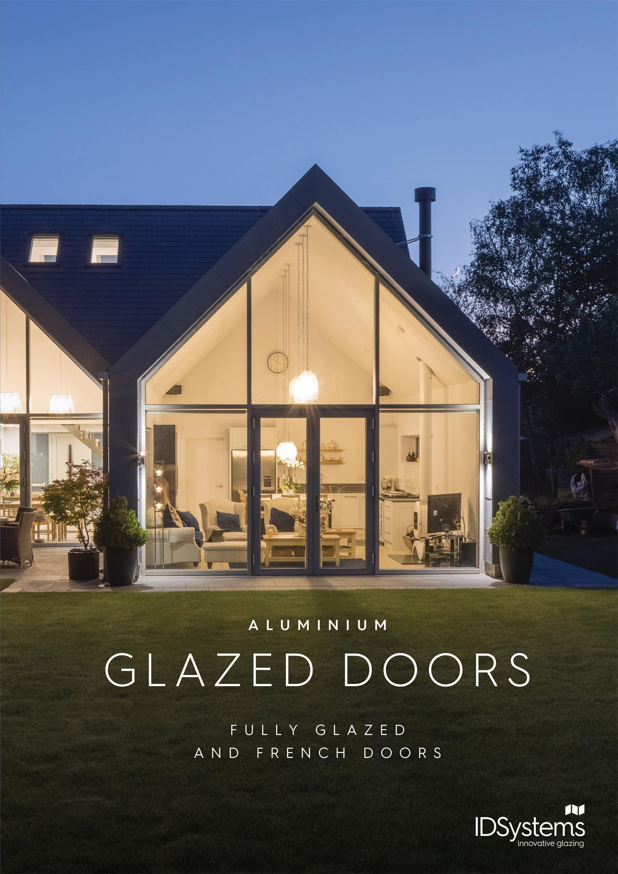 Modern house with large aluminum glazed doors, seamlessly bridging the well-lit interior and lush garden. Discover the elegance of fully glazed and French doors by IDSystems. Explore more through our exclusive downloads for a closer look at innovative design solutions.