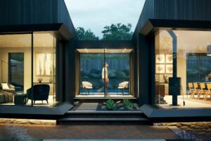 Modern house with large glass windows showing interior rooms; a person is walking inside a glass corridor connecting two sections.