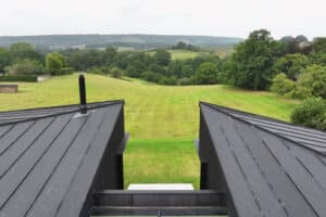 View from a modern black-roofed building overlooking a large, neatly mowed grassy field with trees and hills in the background.