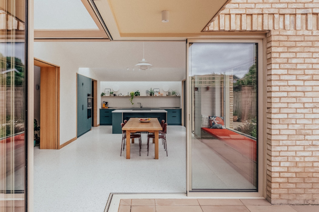 View into a modern kitchen and dining area with a wooden table, chairs, blue cabinets, and large glass sliding doors leading to an outdoor patio.