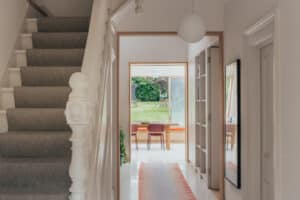 A hallway with carpeted stairs on the left, a runner rug, and a view into a dining area with glass doors opening to a green backyard.