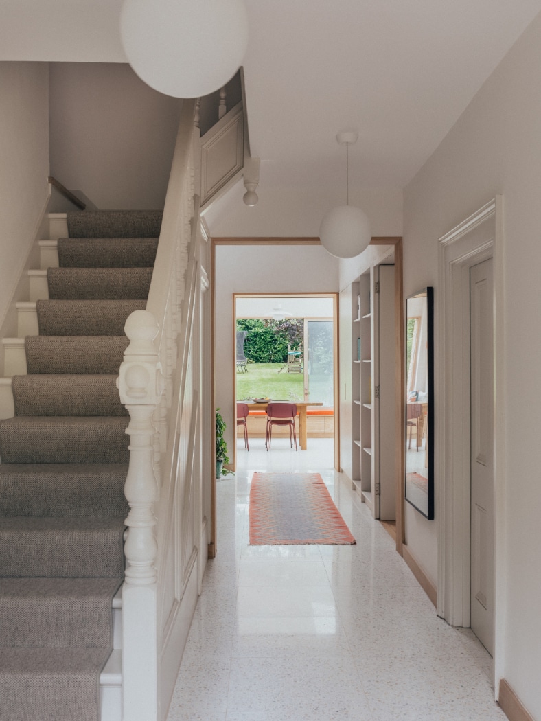 A hallway with carpeted stairs on the left, a runner rug, and a view into a dining area with glass doors opening to a green backyard.