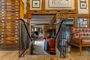 A cozy living room with exposed wooden beams, a wood stove, a mix of modern and rustic furniture, and a wall of labeled drawers on the left.