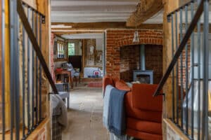 Cozy living room with exposed brick walls, a wood-burning stove, red sofa, and stone floor, viewed through a rustic gate with wooden beams and metal bars.